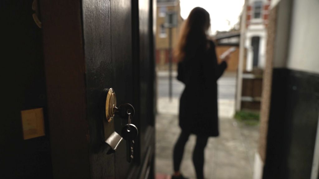 A lock with a key in it is in the foreground. Blurred in the distance is the silhouette of a woman on her mobile phone