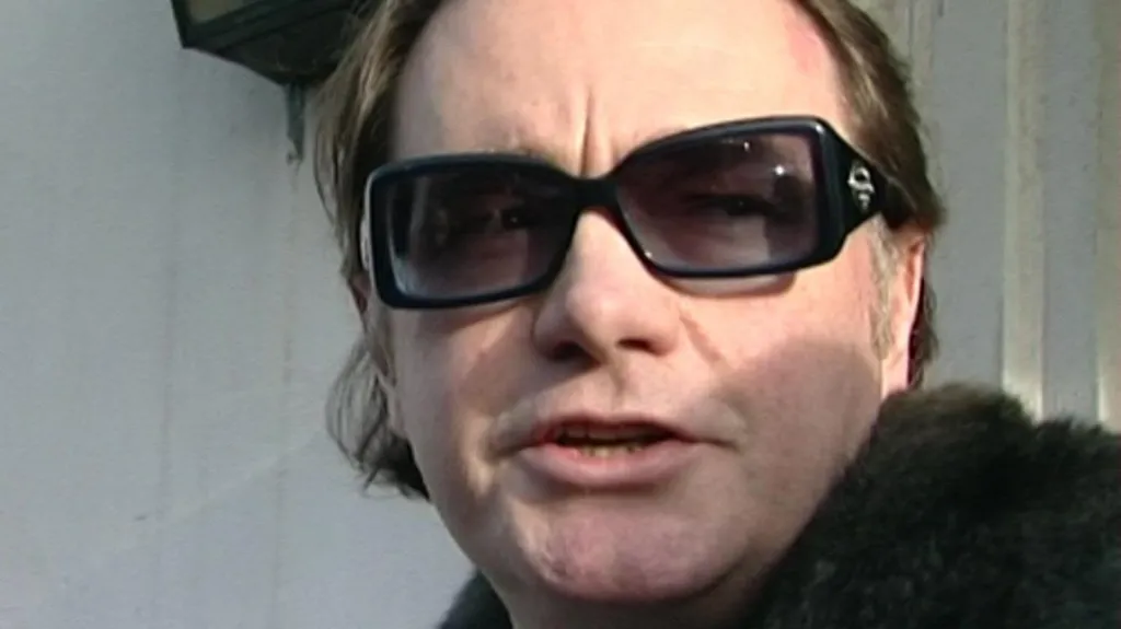 Raymond Scott speaks to the media outside Durham police station. He is wearing large designer black sunglasses and a fur coat, is clean shaven with long brown hair.