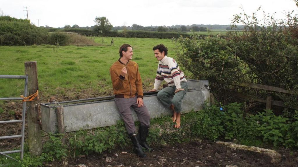 Two men sitting on a cattle trough in a field