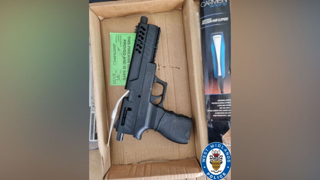 A black air pistol sits inside an open cardboard box alongside a box of hair clippers. A green evidence tag is attached to the weapon with white cable ties, with handwritten text and a label reading "this firearm has been proved and is safe". The West Midlands Police crest is visible in the bottom right corner of the image.