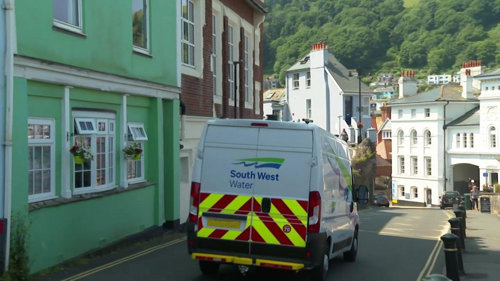 A white van branded with South West Water is driving along a street on a sunny day.