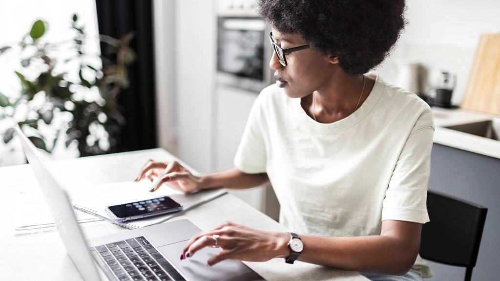 Woman using laptop, notepad, and calculator to look at bills on a white kitchen table