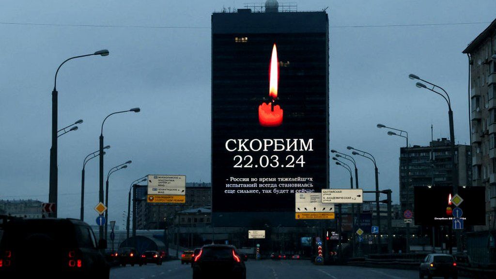 Cars driving past a building in Moscow displaying a lit candle and text reading "Mourn"