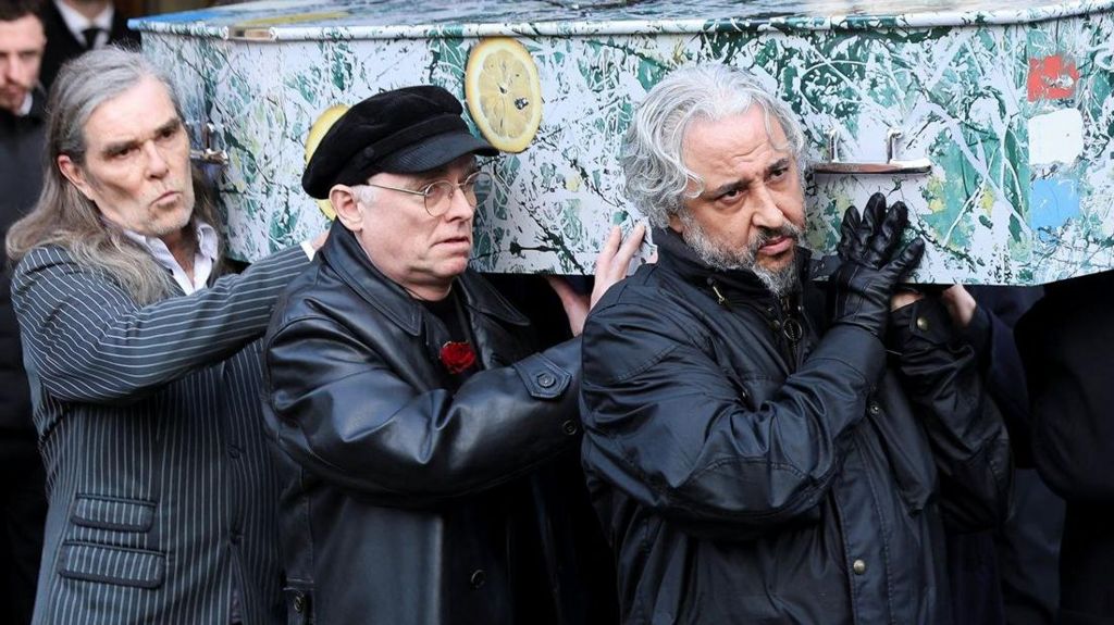 Another picture of Mani's former Stone Roses and Primal Scream bandmates carrying his coffin out of the cathedral.