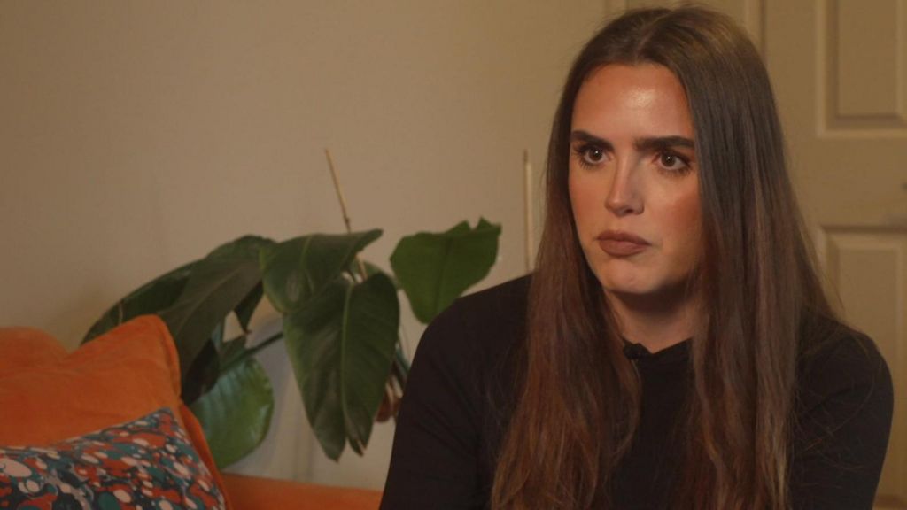 Hannah Strickland is sitting on a large orange sofa with a plant in the background