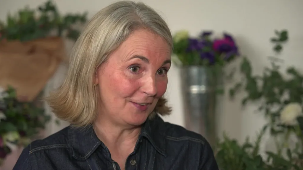 Woman with blonde hair and denim shirt in front of bouquets of flowers