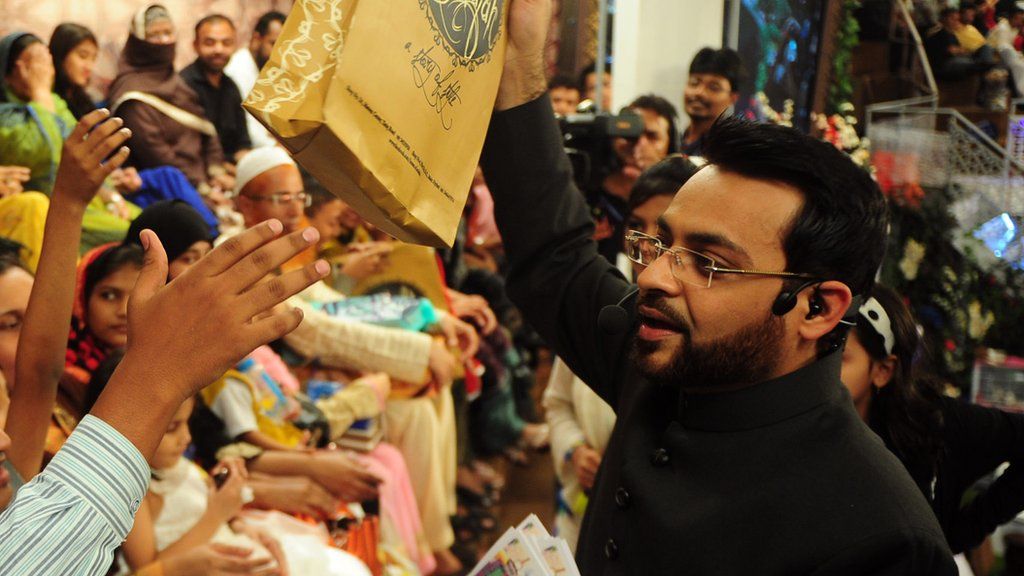 Pakistani television show host Aamir Liaquat Hussain (R) distributes gifts to the audience during an Islamic quiz show