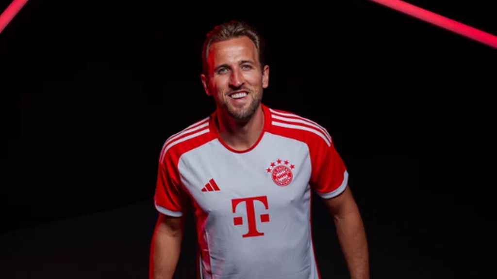  Harry Kane is pictured wearing a red and white Bayern Munich jersey, smiling.