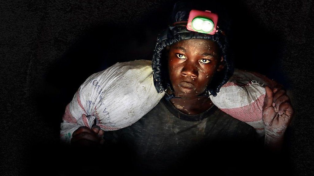 Young boy with a head torch and a heavy sack on his shoulders