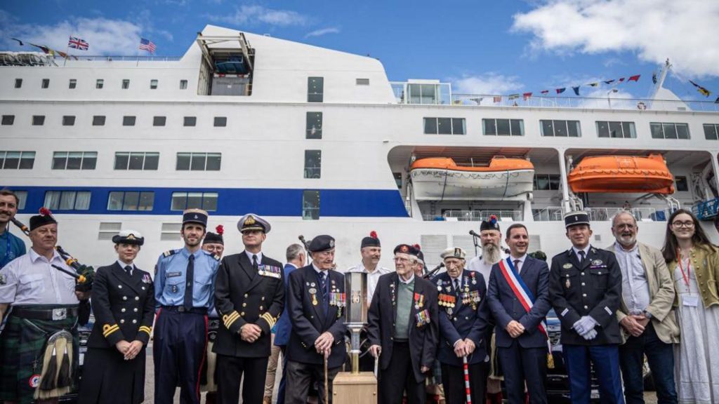 British WWII veterans Stan Ford (C-L), Alec Penstone (C-R) and Jim Grant (C) pose for photographs with the 'Torch of Commemoration' and French and British officials at their arrival at Caen-Ouistreham ferry terminal during a welcome ceremony for the 30 British veterans arriving to participate at the 80th anniversary of D-Day in Normandy, in Ouistreham, France