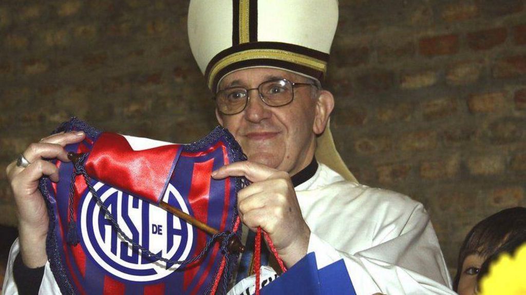 Pope Francis is shown while a bishop in Buenos Aires. He is holding up a football pendant of his favourite team.