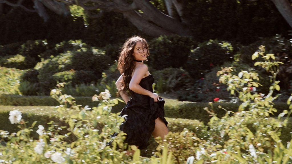 A picture of Laufey running through an ornate garden in a black ballgown