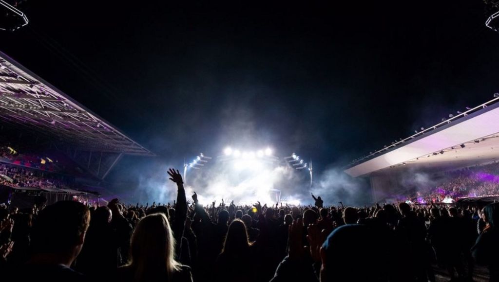 Crowd packed into Ashton Gate stadium as a show takes place, with bright stage lights