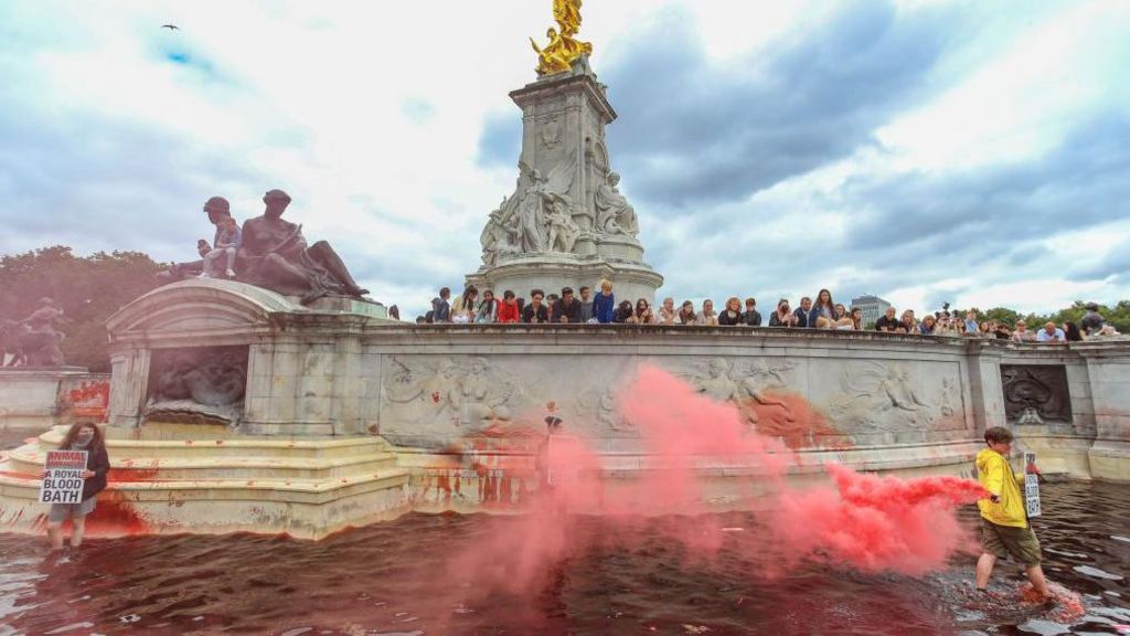 Protesters with red paint flares and signs in the dyed Victoria fountain.