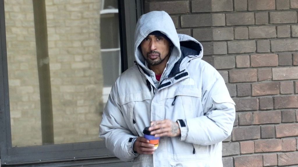 A man wearing a grey hoodie and a grey jacket. He is holding a coffee cup.