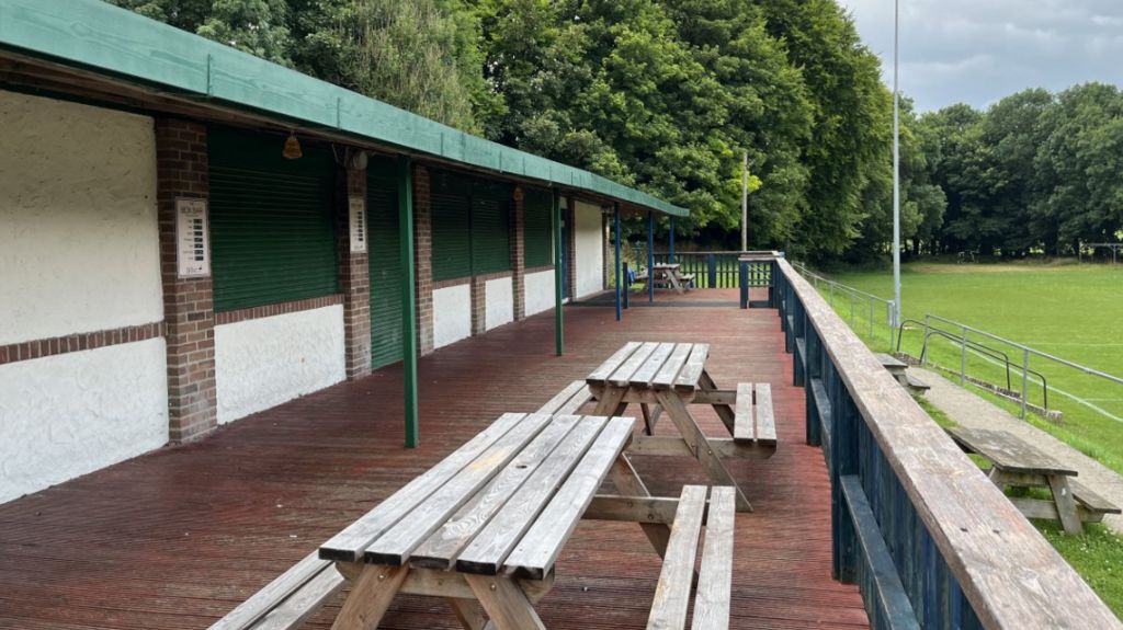 Exterior view of Shrewton United with picnic benches and wall near to pitch.