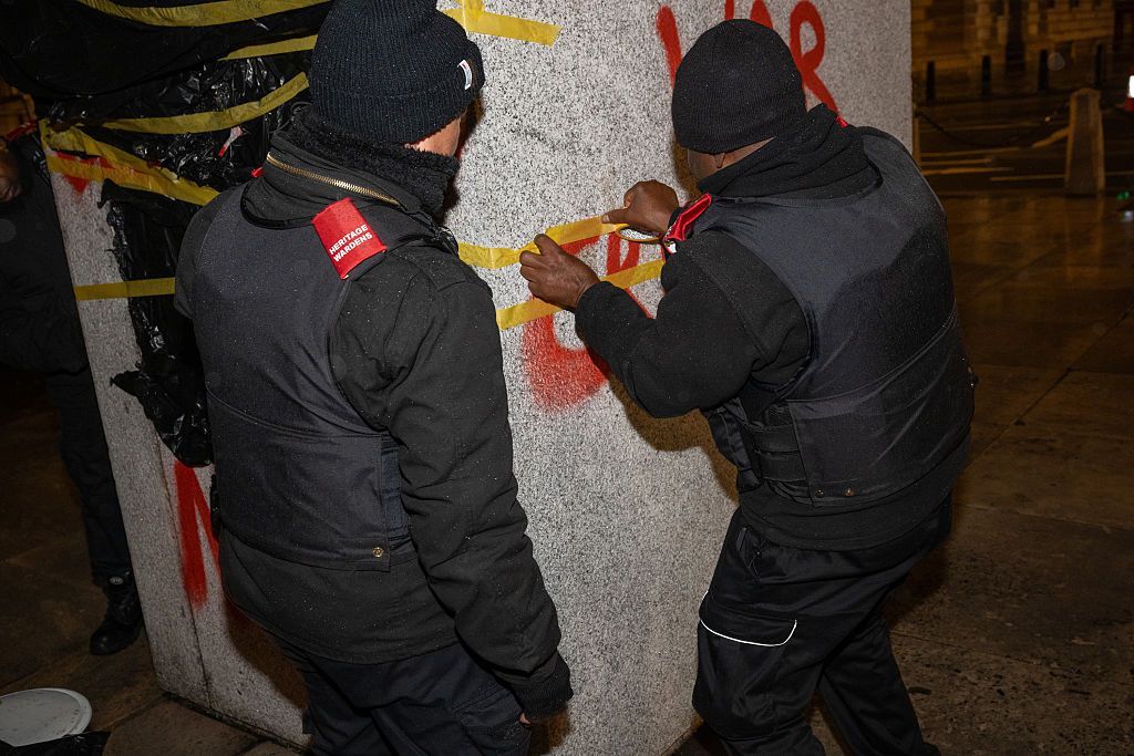 Two men dressed in black cleaning the statue's plinth