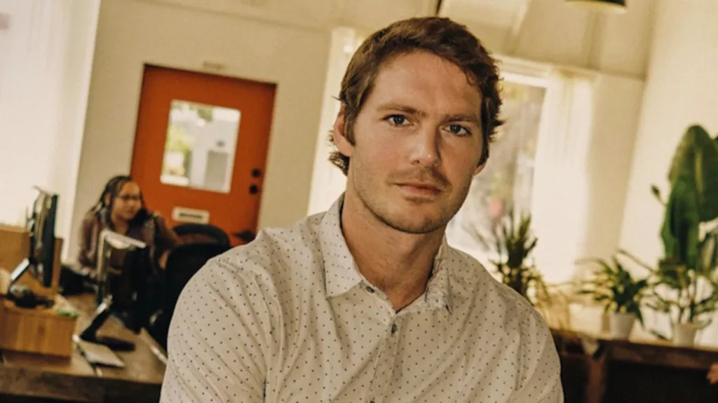 Graham Dugoni sits with his arms folded and looking directly at the camera. He is wearing a white shirt with black polka dots.