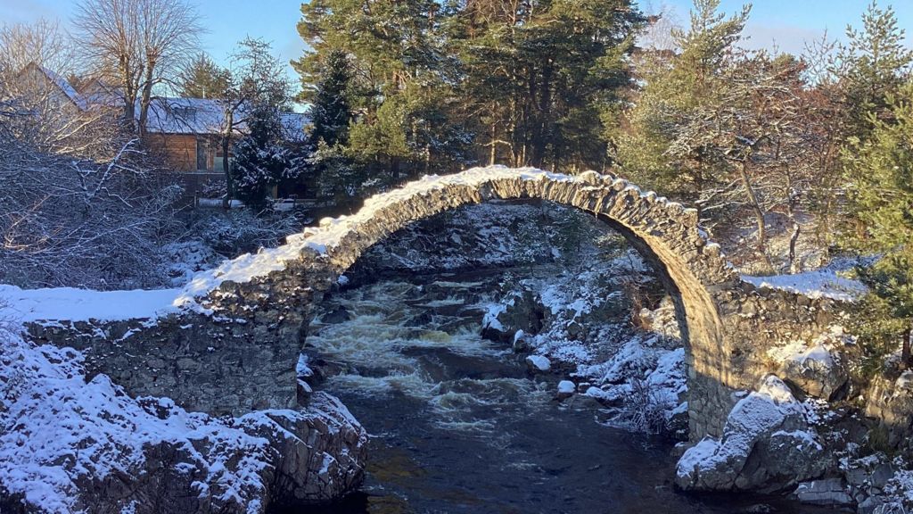 Snow covers a stone bridge over a body of water