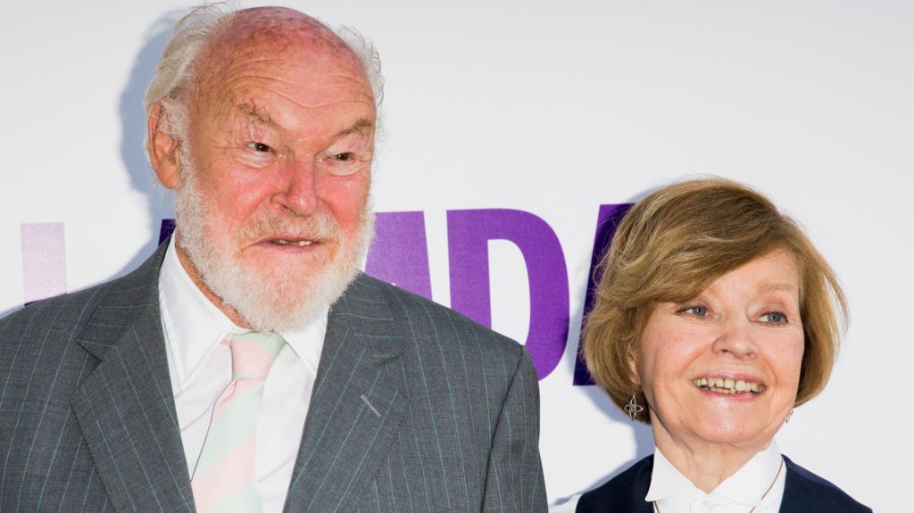 Timothy West, wearing a white shirt and grey jacket, alongside Prunella Scales, who is wearing a white shirt and black waistcoat.