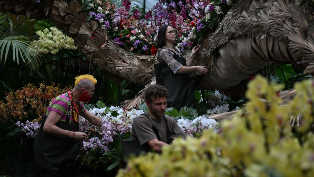 Three horticulturalists arrange orchid arrangements on and around the dragon sculpture 