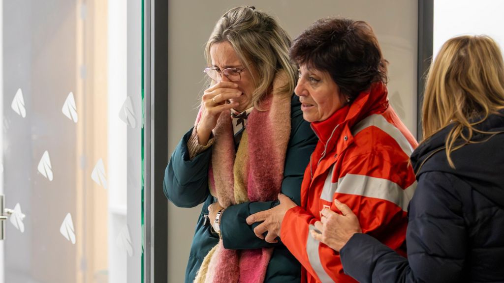A woman is consoled by a woman wearing a fluorescent official jacket at the terminal of a train station