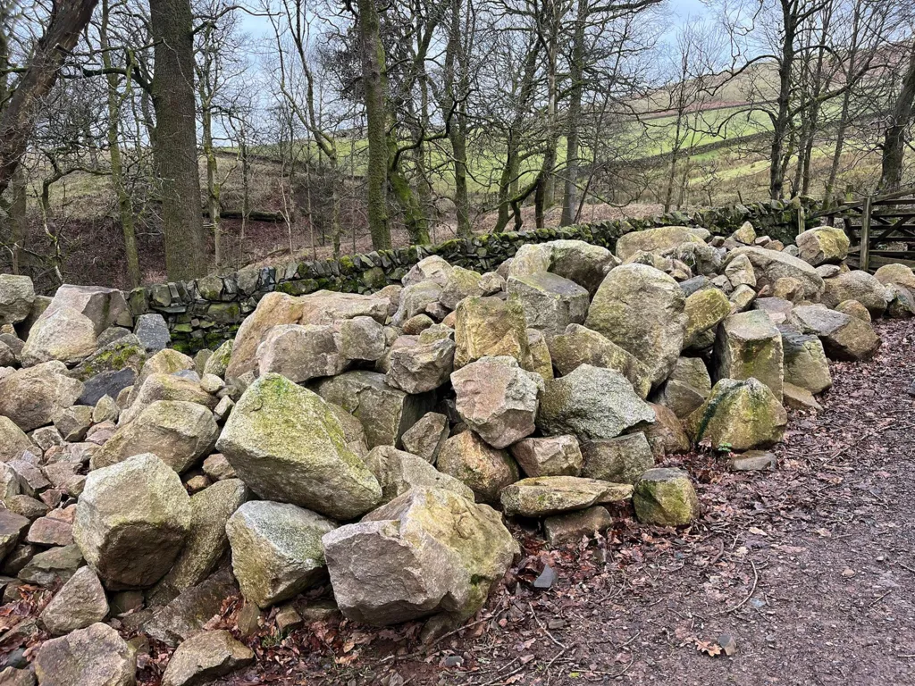 A pile of large stones place by a wall on a muddy path 