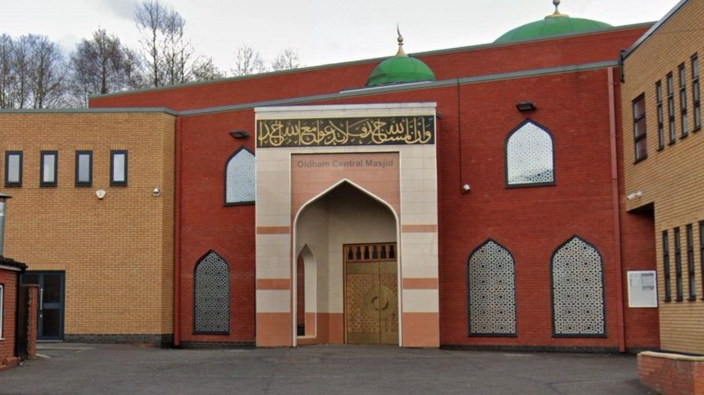 The red and sand-coloured brick-built front of Oldham Central Mosque, with arched windows covered in detailed patterns