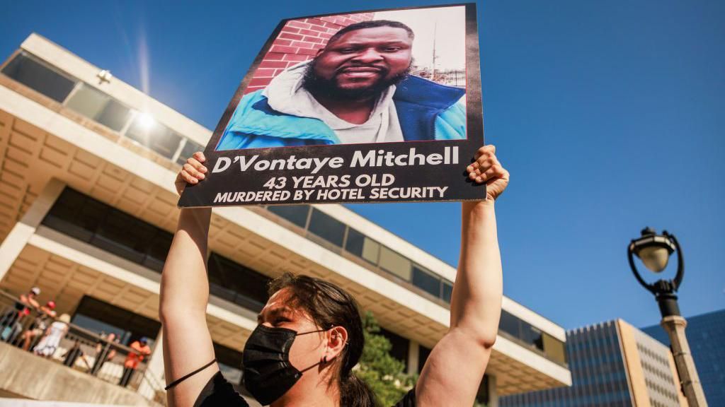 A woman holds up a sign showing D’Vontaye Mitchell after his death 