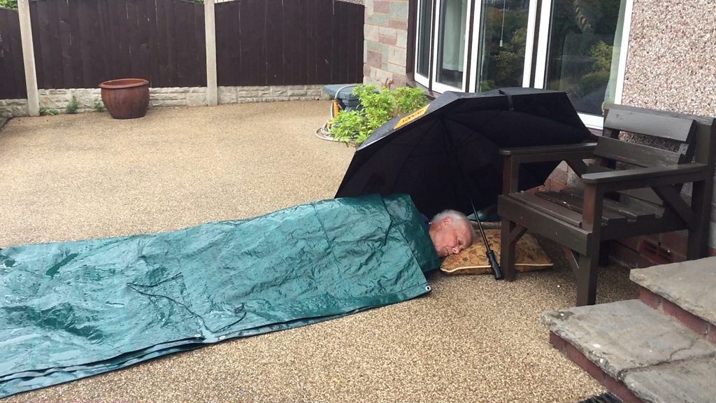 Man lying on driveway covered by tarpaulin