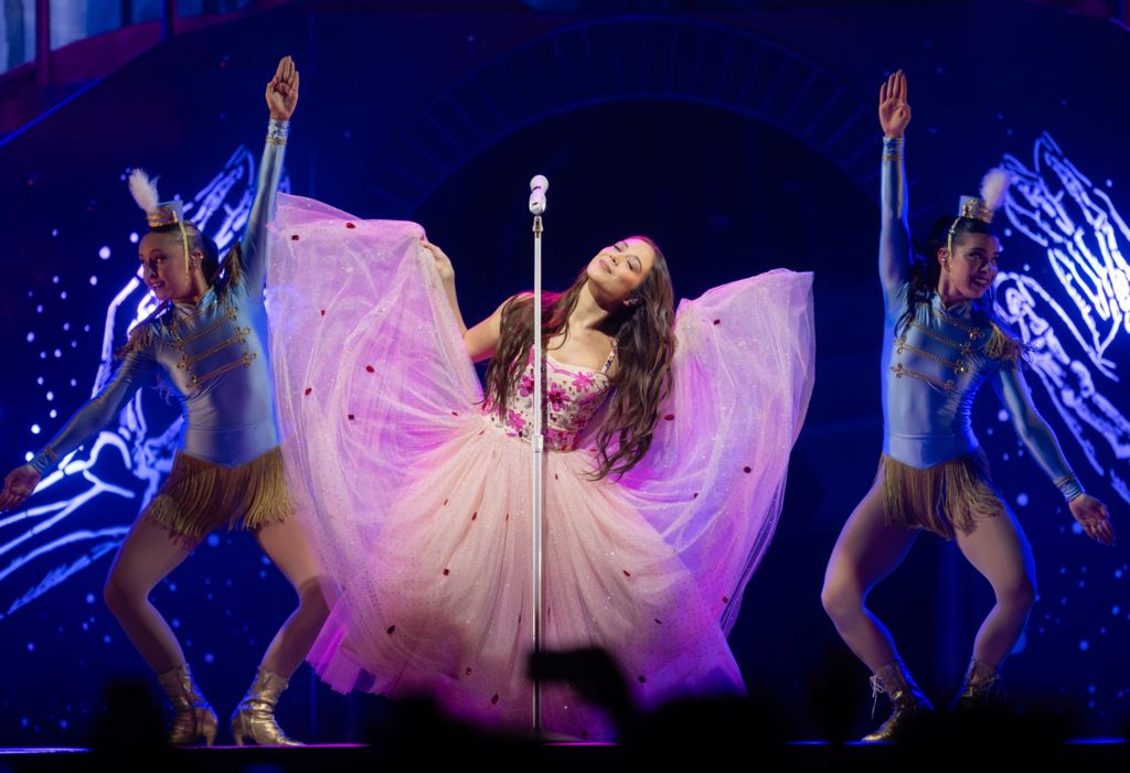 Laufey lifts up the chiffon "wings" of her pink ballgown, while performing on stage at London's O2 Arena in March 2026