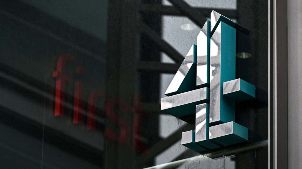 A file photo shows the Channel 4 logo on the side of a building at the headquarters of the broadcaster, draped in shadow on a cloudy day.