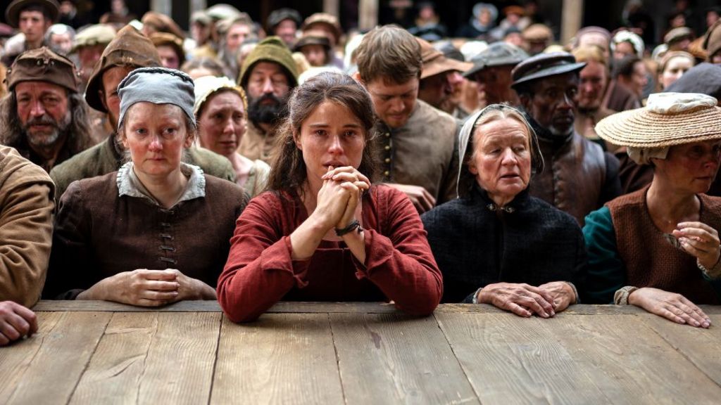 Jessie Buckley in Hamnet, putting her hands to her mouth, surrounded by people