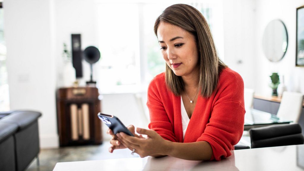 a woman in a red cardigan looks at her phone