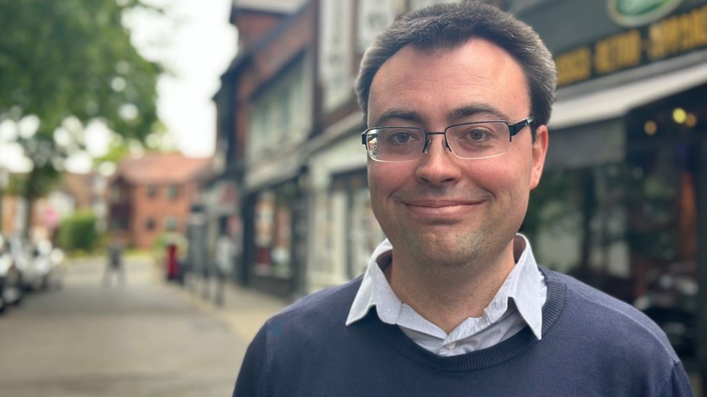 Laurence Turner MP in a shirt and blue jumper standing in the street