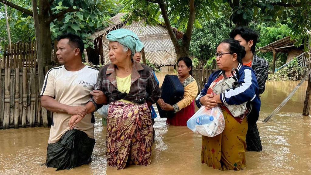 Residents stand in flood waters with their belongings in Sin Thay village in Pyinmana, in Myanmar's Naypyidaw region, on September 13, 2024, following heavy rains in the aftermath of Typhoon Yagi. 