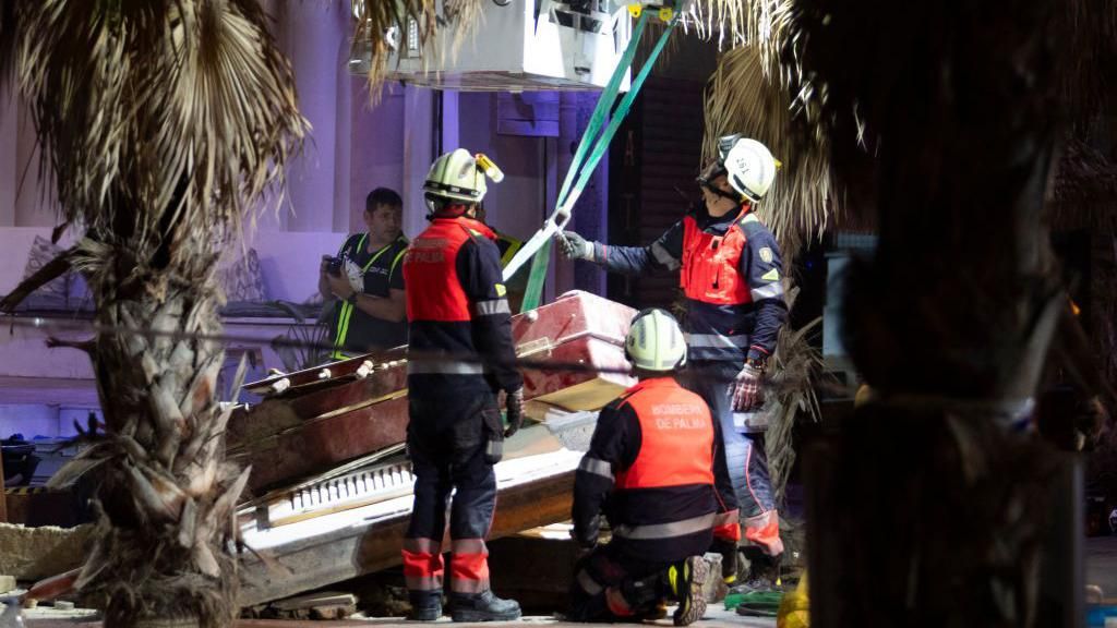 People in hi-vis vests and hard hats surrounded by rubble