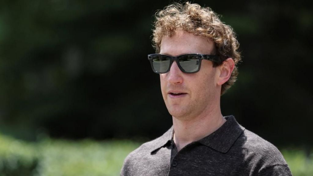 Zuckerberg, wearing black sunglasses and a dark polo shirt, outisde with a green background