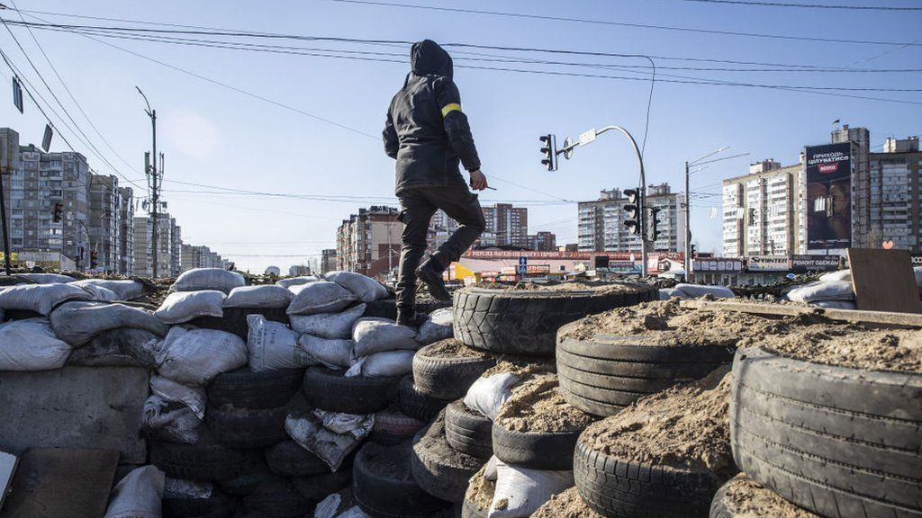 A man stands on a barricade made of sandbags and tyres