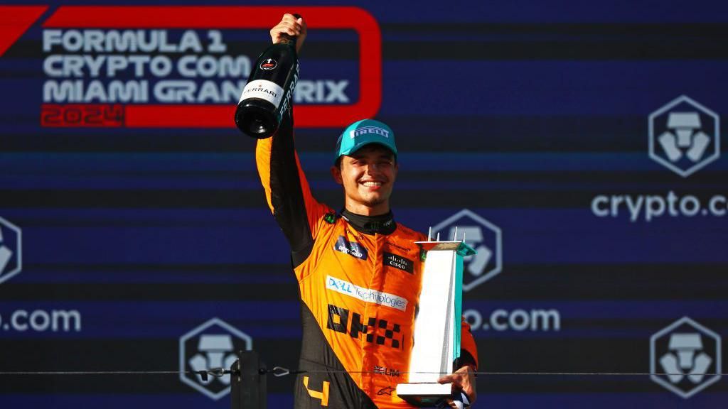 Lando Norris holds his winners' trophy and a bottle of champagne on the podium after the Miami Grand Prix