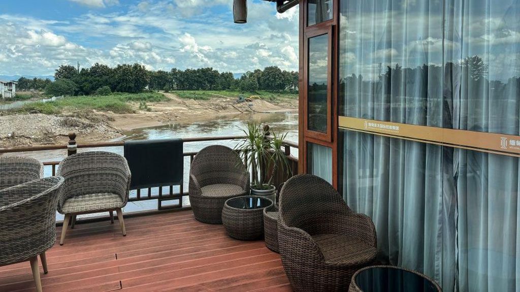 A view of the villa that is being used by He Yingxiong who is currently running Shwe Kokko. A decking area with woven chairs overlooks a river and green trees on the other side