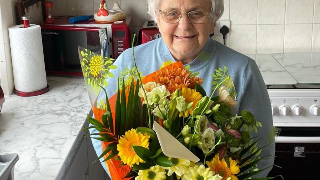 An elderly woman holds a bouquet of brightly coloured flowers