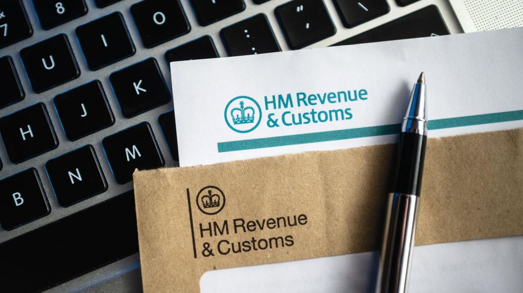 An HMRC-headed envelope and letter with a pen on top and a computer keyboard underneath.