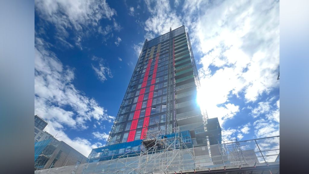 The outside view of the large tower block, with the sun shining, and scaffolding visible all over