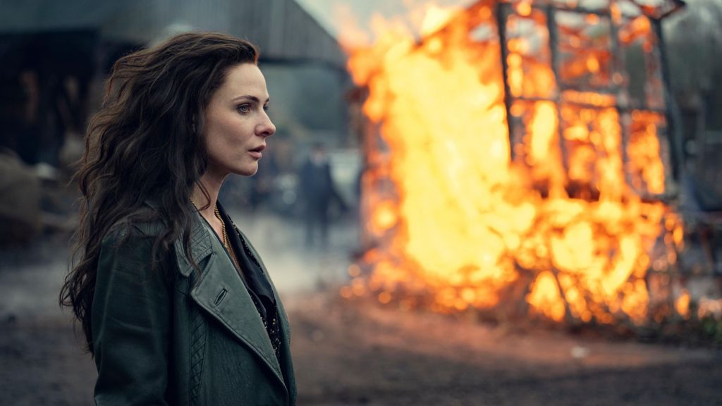 Rebecca Ferguson standing in front of a burning structure in a scene from the film