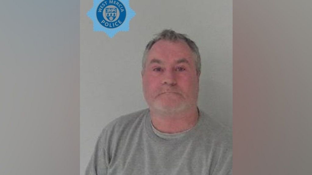 Dave Butler in a police photo. He is wearing a grey top and looking at the camera. He has grey hair and grey stubble and the West Mercia Police logo is printed on the photo to the top left. 