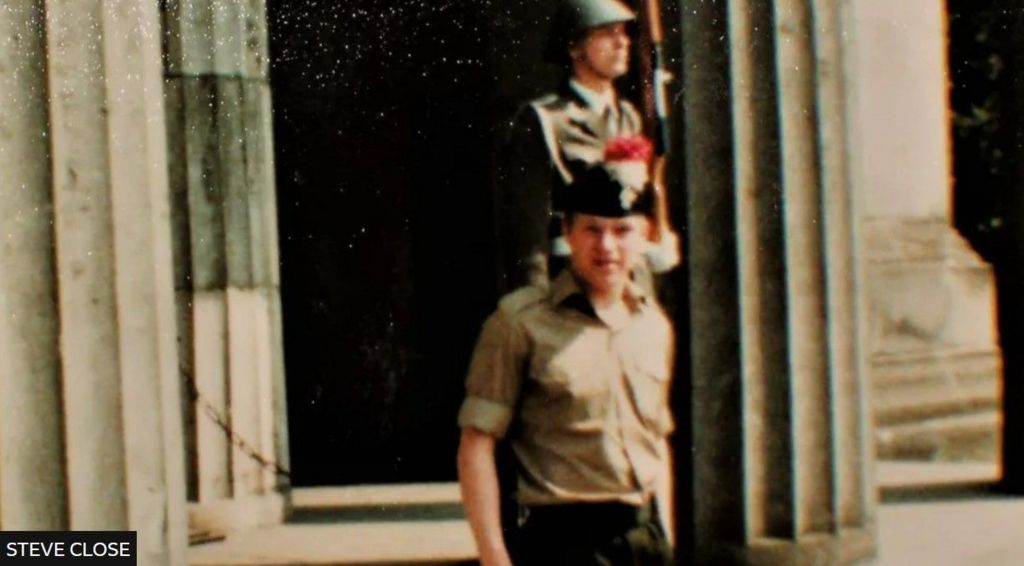 Steve Close in Berlin in his uniform, with an armed soldier in the background 