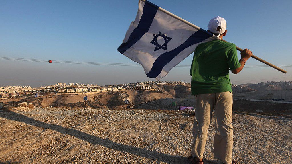 Boy holds Israeli flag with settlement in background (file photo)