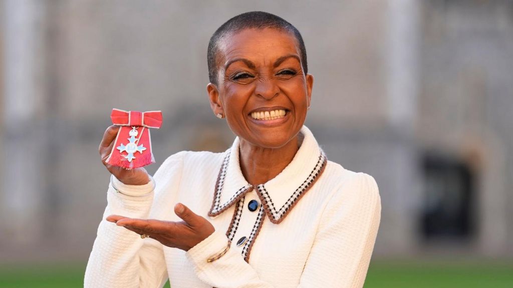 A woman in a white dress holding up a Member of the Order of the British Empire award.