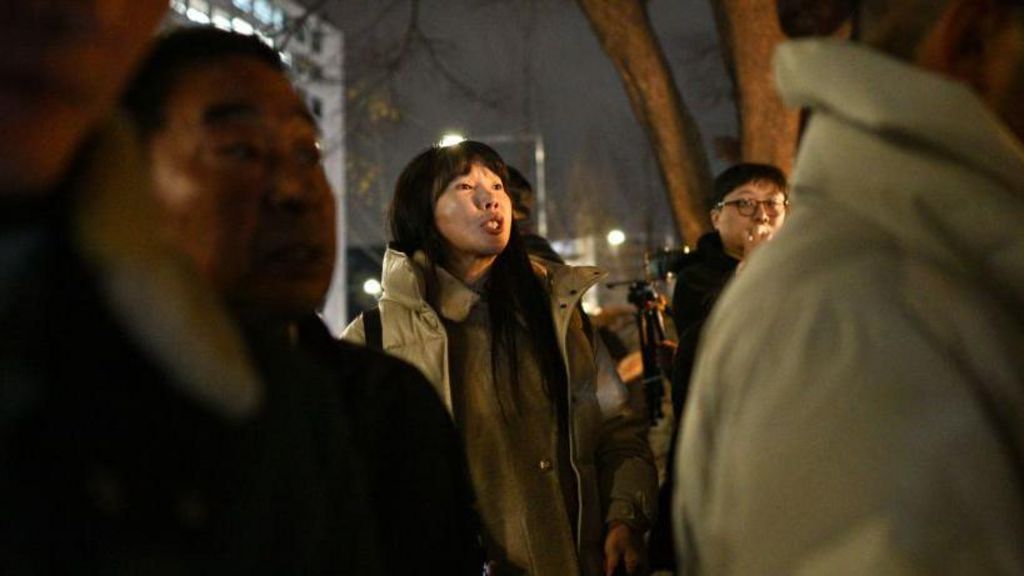 A woman with a beige coat and long black hair shouts slogans as she protests outside parliament in Seoul
